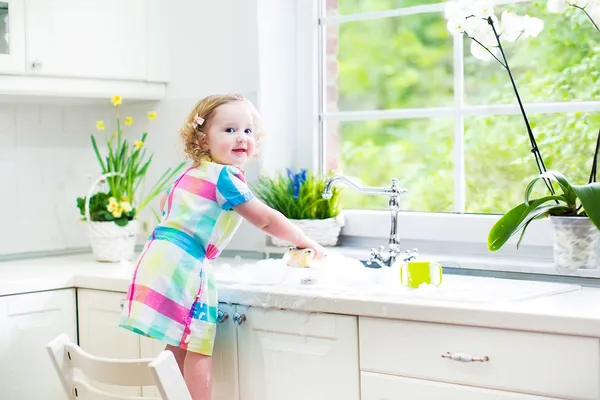 Девушка мило кудрявый малыш в красочное платье, мытье посуды — стоковое фото