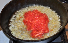 Переменив огонь конфорки на средний, пассеруем 7-8 минут лук, временами помешивая. Тем временем разрезаем пополам помидоры и быстро натираем на крупной терке. И всю эту томатную массу выливаем в сковороду. Приправляем солью и перцем чили, кориандром, порубленным мелко чесноком. Тушим под крышкой 4-5 минут.